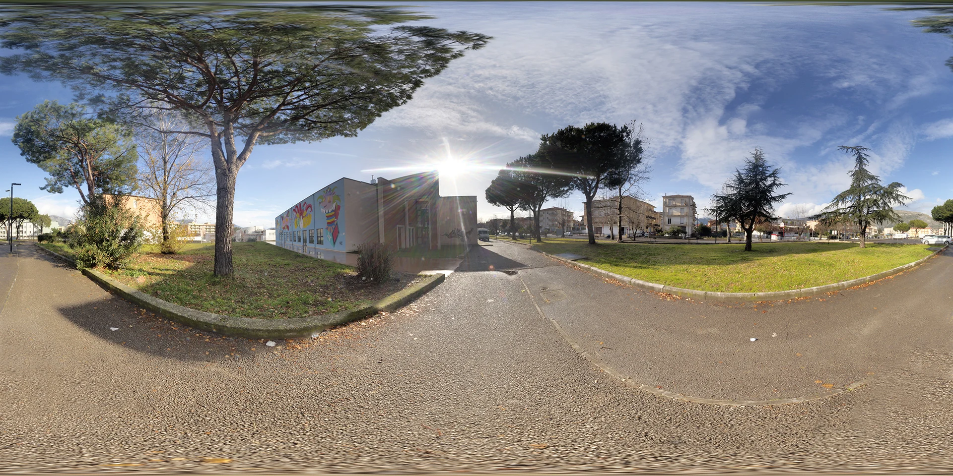 Buildings, Trees and Street Art HDRI preview: a paved walkway passes grass, tall trees and a low mural-covered building beneath sun and wispy clouds.